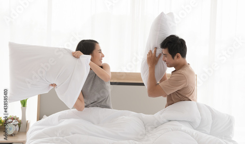 Cheerful ethnic couple fighting with pillows on bed © Bangkok Click Studio