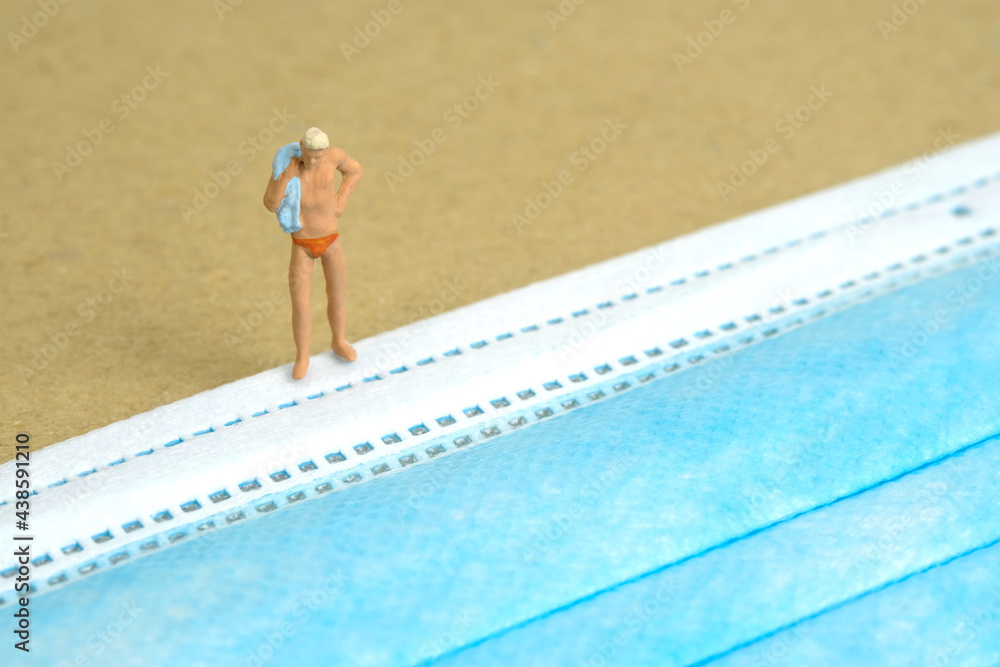 Miniature people toy figure photography. Safety travel concept, Men with swimsuit standing in front of blue face mask