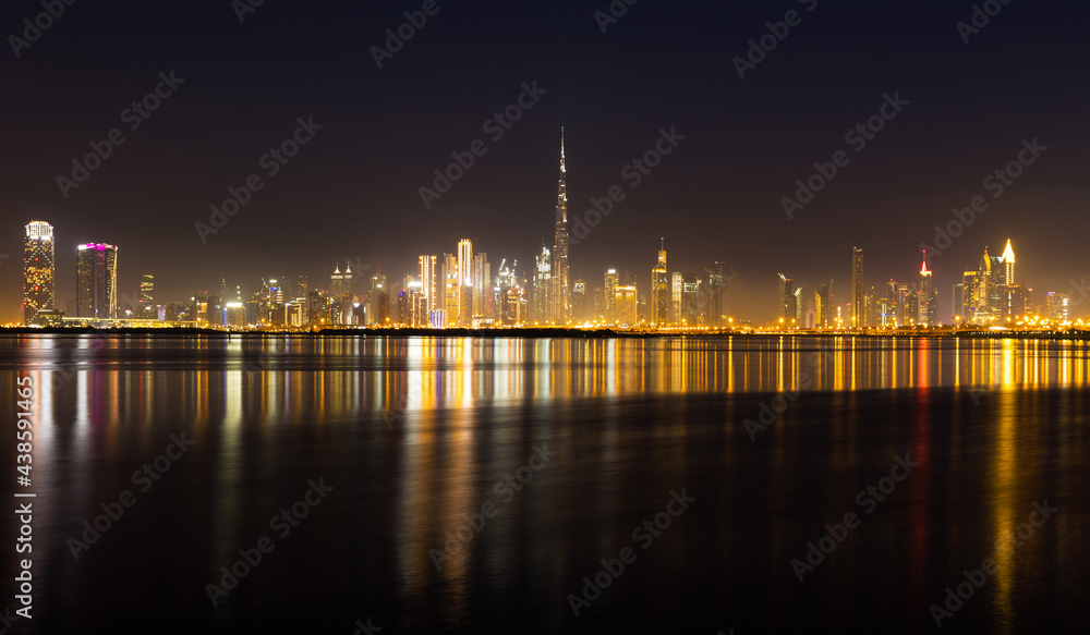 Night view of Dubai city skyline with reflections on the water.