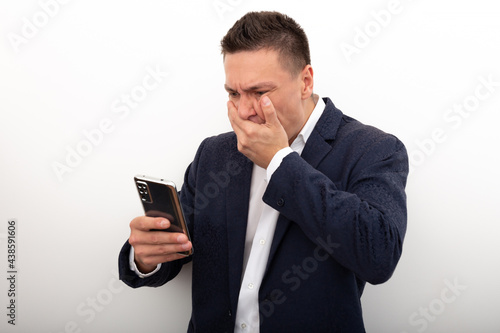 A business man in a jacket and white shirt uses a mobile phone, looks with horror at the screen of his smartphone, Very bad news, a terrible situation has happened. Negative emotions