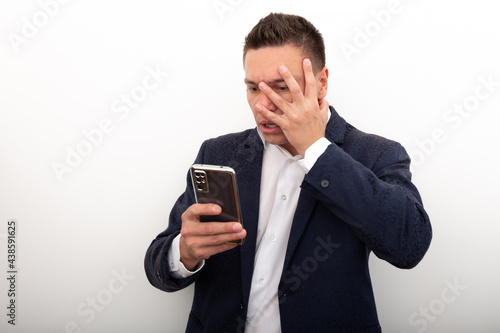 A business man in a jacket and white shirt uses a mobile phone,looks with horror at the screen of his smartphone, Very bad news, a terrible situation has happened. Negative emotions on a person's face