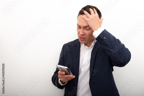 A business man in a jacket and white shirt uses a mobile phone, looks with horror at the screen of his smartphone, Very bad news, a terrible situation has happened. Negative emotions on a person's