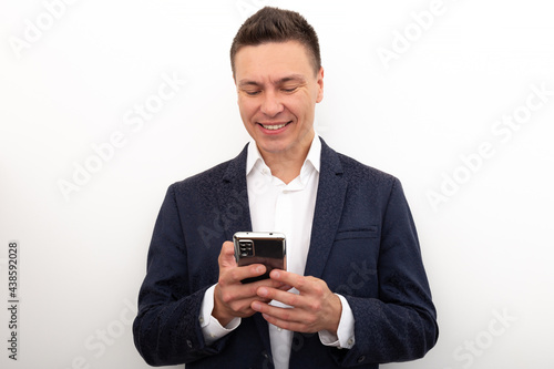 Business man in a jacket and white shirt uses a mobile phone, shows his joy and delight, rapture in a selfie camera, on a white background © Anton Prokopenko