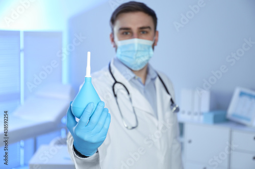 Doctor holding rubber enema in examination room  focus on hand. Space for text