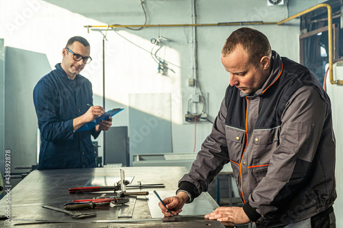 Obraz na plátně A tinsmith is sketching in his workshop with a colleague engineer who is taking