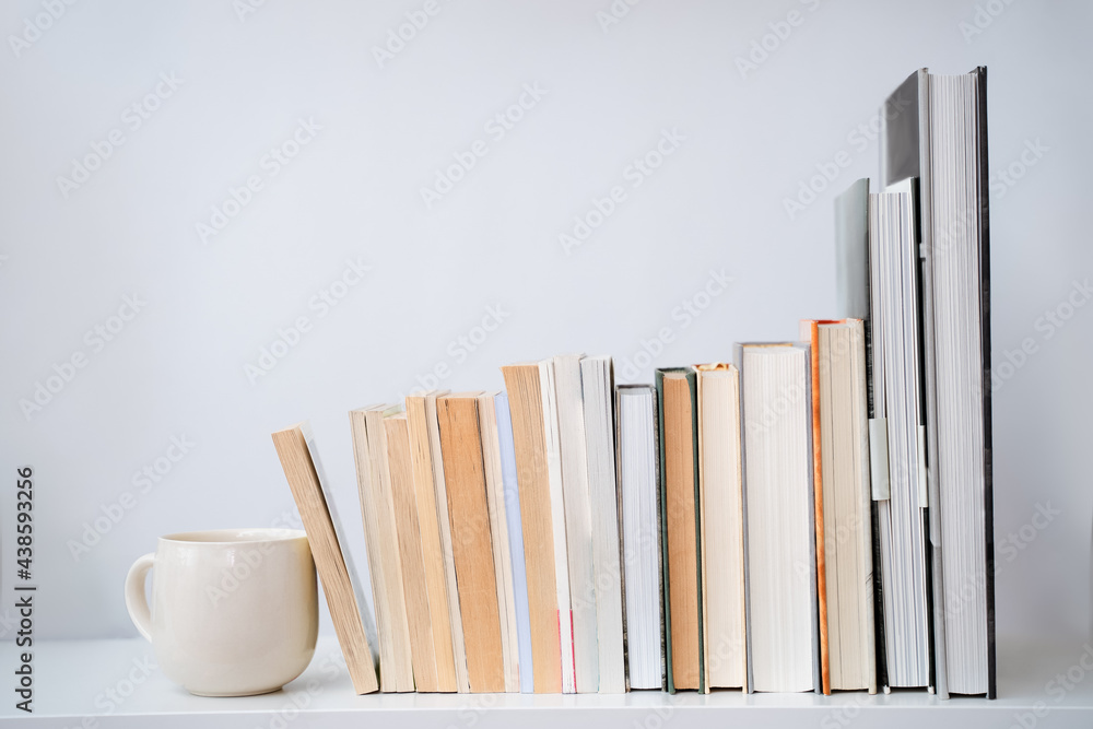 Naklejka premium coffee cup tea mug next to a stack of books. White table and background. Front view