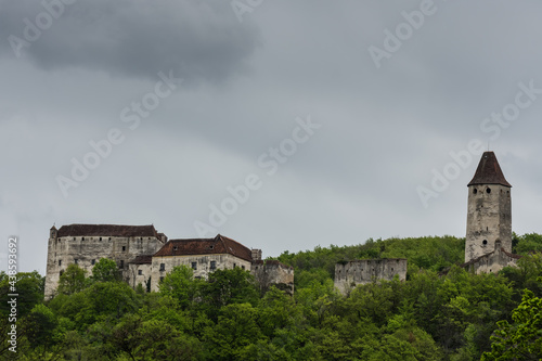 old castle with a tower between many green trees and grey sky