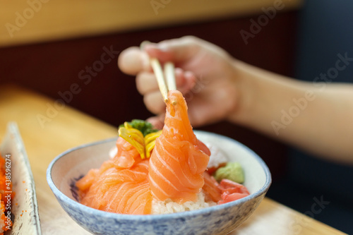 Asian woman eating salmon slice sashimi with rice in Japanese restaurant