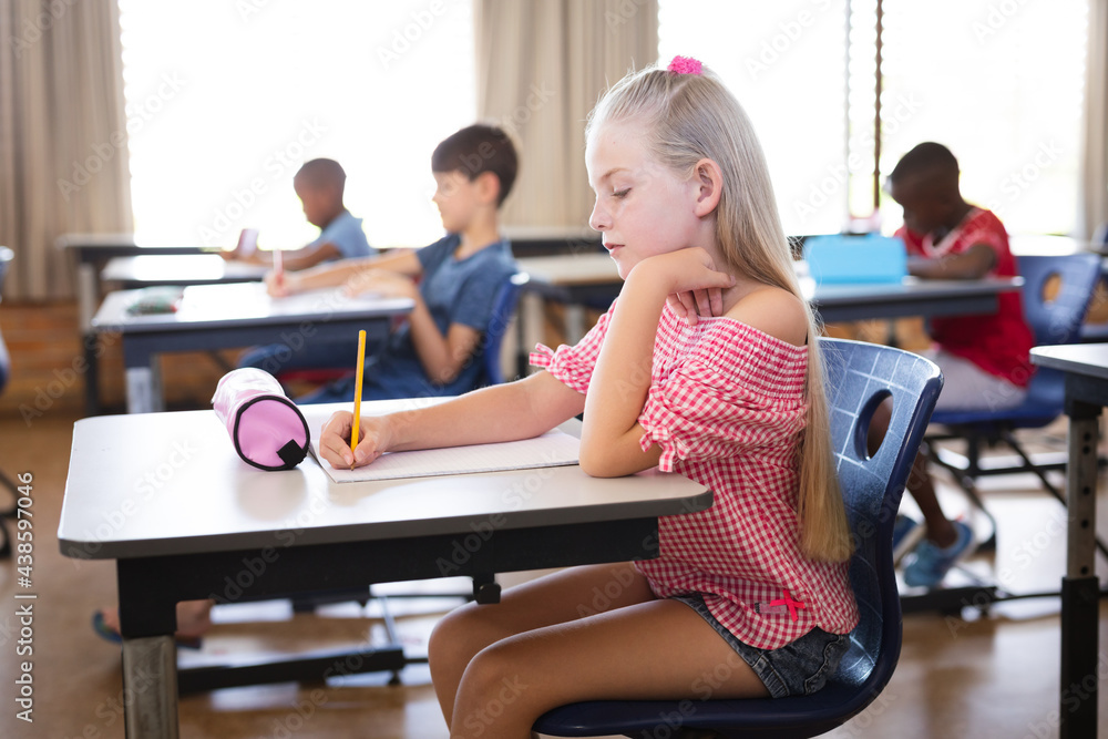 Caucasian girl studying while sitting on her desk in the class at school Caucasian girl studying while sitting on her desk in the class at school