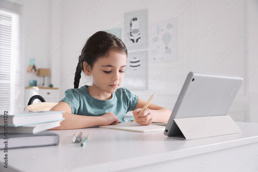 Little girl doing homework with tablet at table in room Little girl doing homework with tablet at table in room