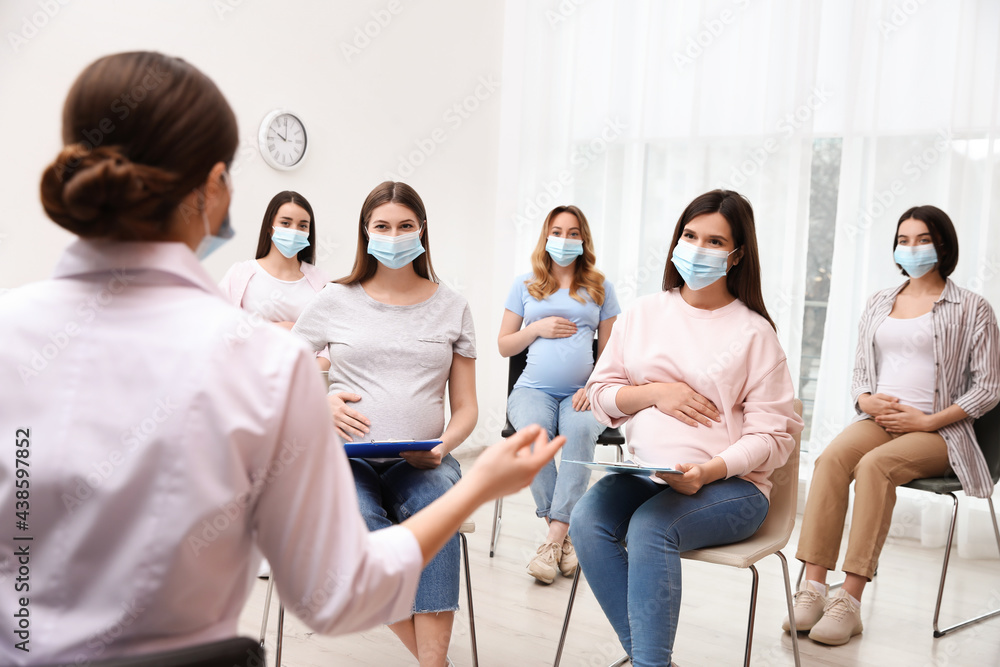 Group of pregnant women in protective masks with doctor at courses for expectant mothers indoors Group of pregnant women in protective masks with doctor at courses for expectant mothers indoors