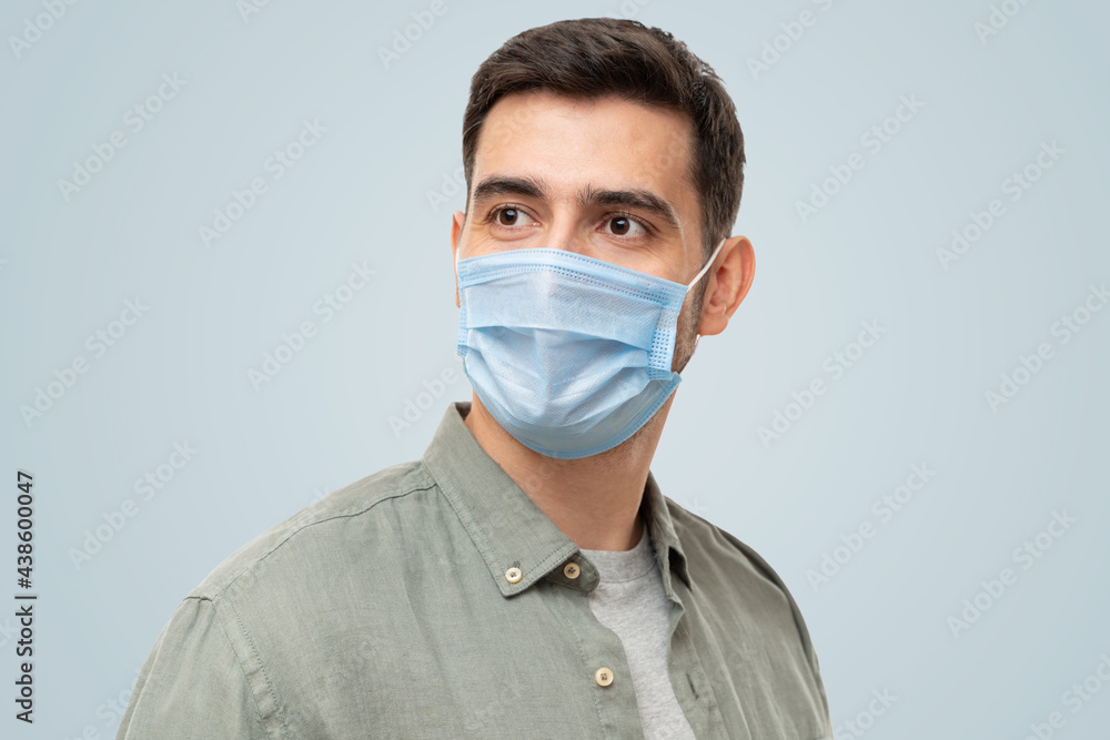 Young man wearing shirt and medical mask standing looking aside Young man wearing shirt and medical mask standing looking aside