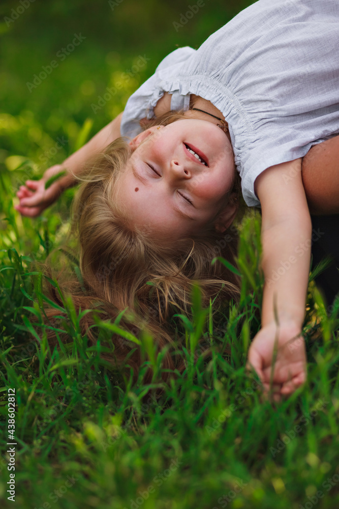 beautiful little girl hanging upside down and relaxing on the background of green grass. beautiful little girl hanging upside down and relaxing on the background of green grass.