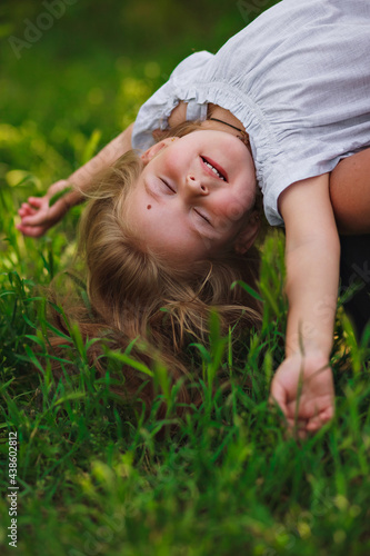 beautiful little girl hanging upside down and relaxing on the background of green grass.
