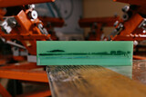 selective focus photo of the rubber part of the squeegee on wooden shelve of the print screening apparatus. serigraphy production. printing images on t-shirts by silkscreen method in a design studio