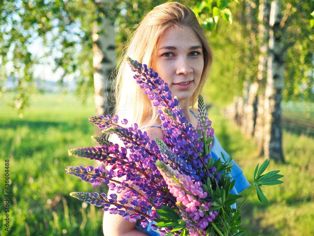 Beautiful girl holding bouquet of summer flowers of purple lupins. Young happy woman enjoying nature. Hello summer. Wellness, harmony and freedom Beautiful girl holding bouquet of summer flowers of purple lupins. Young happy woman enjoying nature. Hello summer. Wellness, harmony and freedom