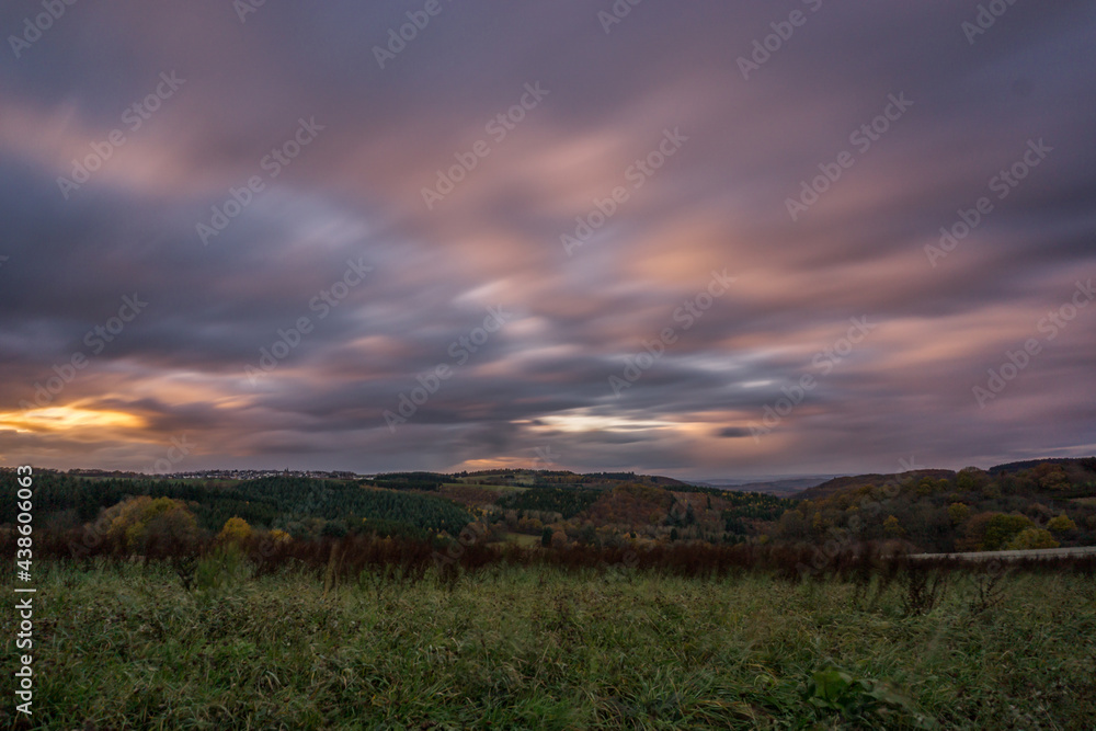 long exposure of german landscape of Hunsrueck in autumn with thick colorful clouds at sunset in the evening