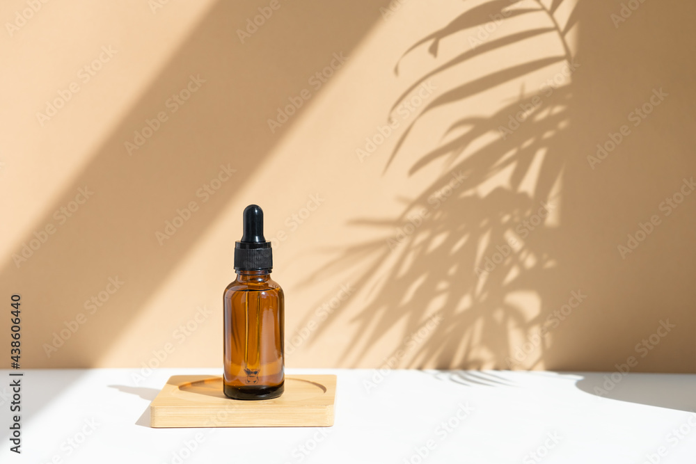 Reusable dark amber glass bottle for oil, cream, lotion or serum on a beige background with a shadow of tropical palm leaves. Presentation of a cosmetic product. Layout of the beauty salon branding.