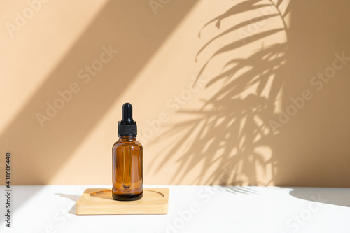 Reusable dark amber glass bottle for oil, cream, lotion or serum on a beige background with a shadow of tropical palm leaves. Presentation of a cosmetic product. Layout of the beauty salon branding. photo