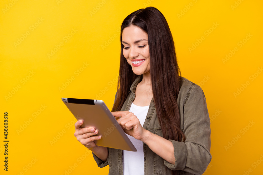 Photo of cheerful nice pretty young woman hold hands look tablet smile isolated on shine yellow color background Photo of cheerful nice pretty young woman hold hands look tablet smile isolated on shine yellow color background