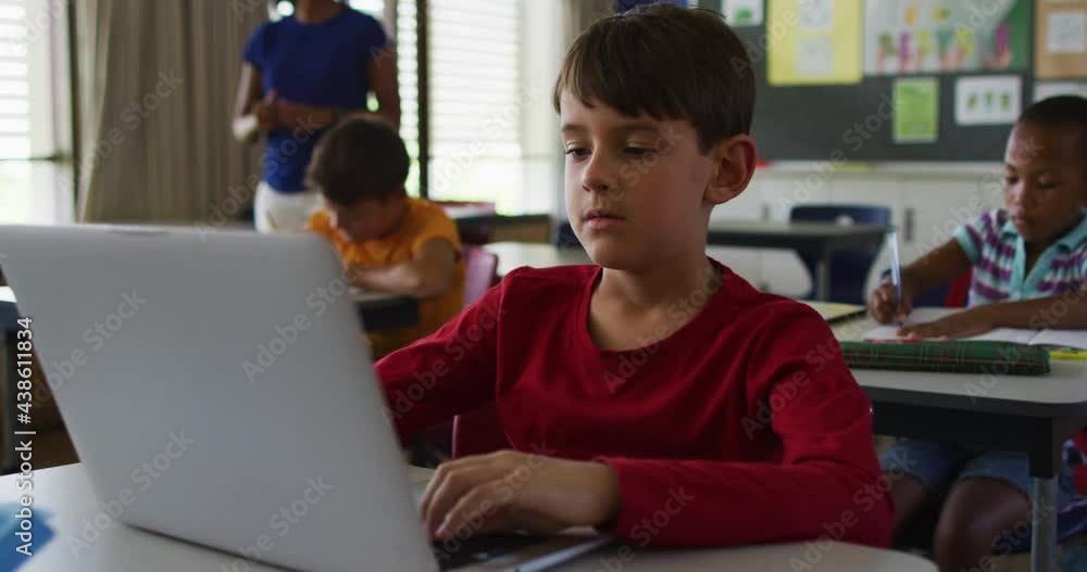 Portrait of happy caucasian schoolboy sitting at classroom, using laptop, looking at camera Portrait of happy caucasian schoolboy sitting at classroom, using laptop, looking at camera