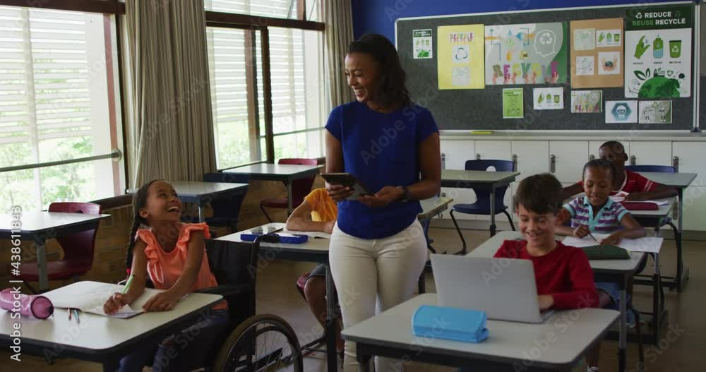 Happy diverse female teacher with tablet and schoolchildren during lesson in classroom Happy diverse female teacher with tablet and schoolchildren during lesson in classroom