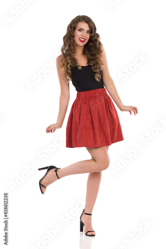 Happy Young Woman In Brown Mini Skirt And High Heels Is Standing On One Leg