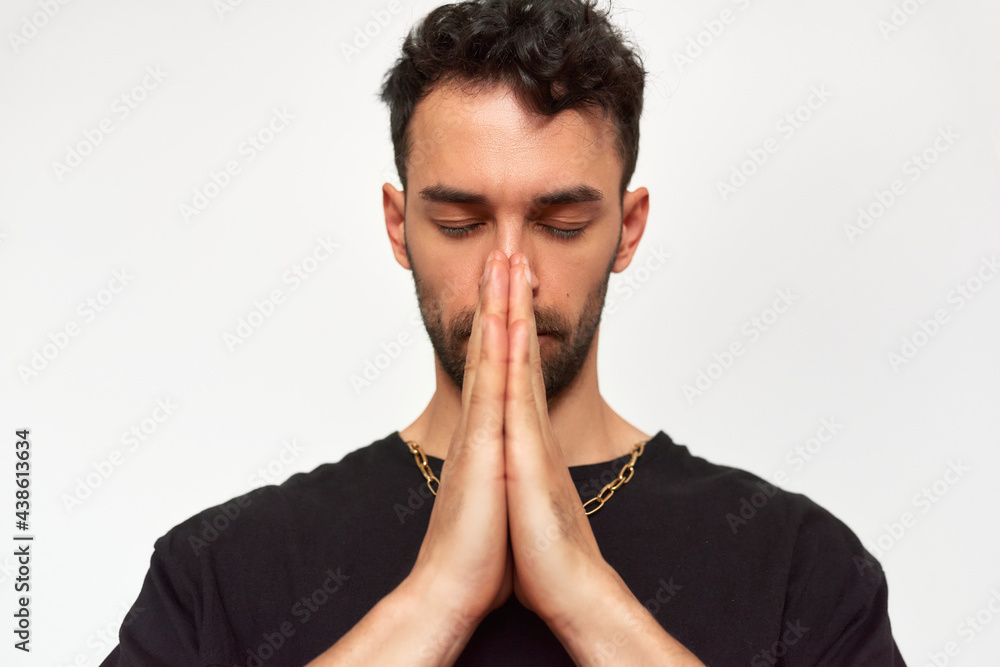 Studio portrait of young man praying with closed eyes in pray gesture with hands, isolated on grey background. Male in black t-shirt has pensive expression. Studio portrait of young man praying with closed eyes in pray gesture with hands, isolated on grey background. Male in black t-shirt has pensive expression.