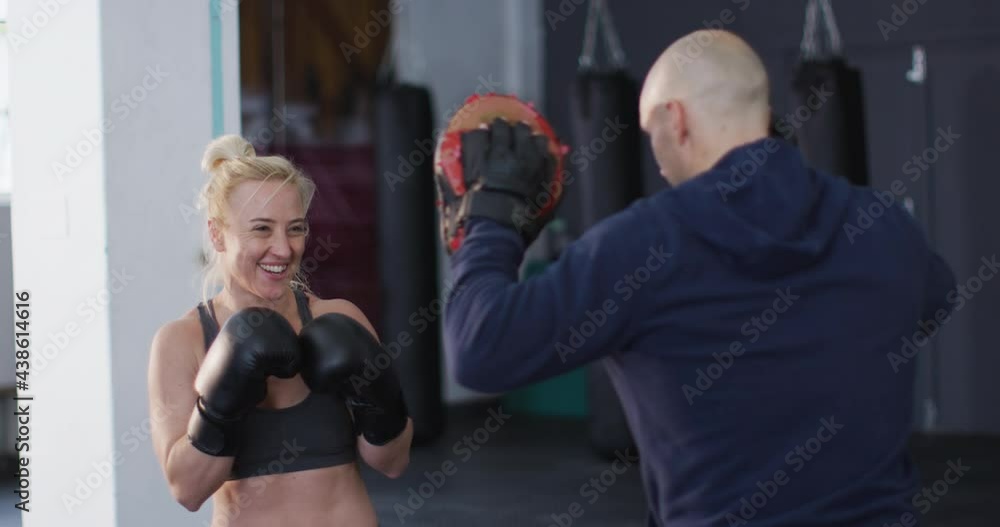 Caucasian female boxer wearing boxing gloves training her punches with male trainer at the gym Caucasian female boxer wearing boxing gloves training her punches with male trainer at the gym