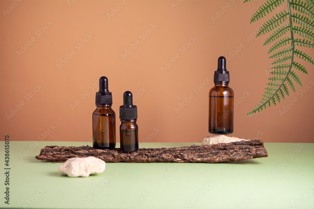 Serum glass bottle set on brown and green background. Composition with natural materials: tree bark, fern leaf and stones. Health and natural care cosmetics concept. Toned image Serum glass bottle set on brown and green background. Composition with natural materials: tree bark, fern leaf and stones. Health and natural care cosmetics concept. Toned image