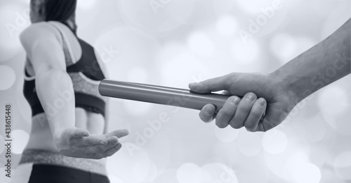 Black and white image of hand passing a baton to female athlete against spots of bokeh lights
