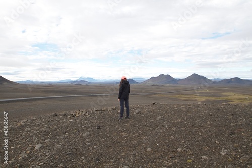 Young girl with long brown hair wears black clothes and colorful hat  admires the landscape in the north of Iceland by the roadside