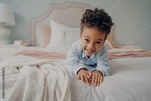 Happy curly afro american boy laying on bed and smiling at camera