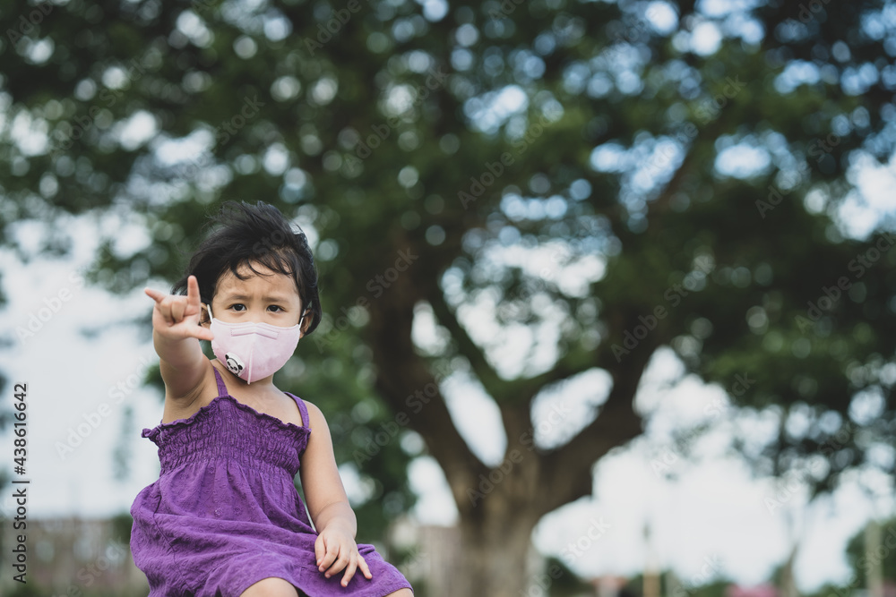 Adorable Little girl wearing protective face mask sitting against tree outdoor. Adorable Little girl wearing protective face mask sitting against tree outdoor.