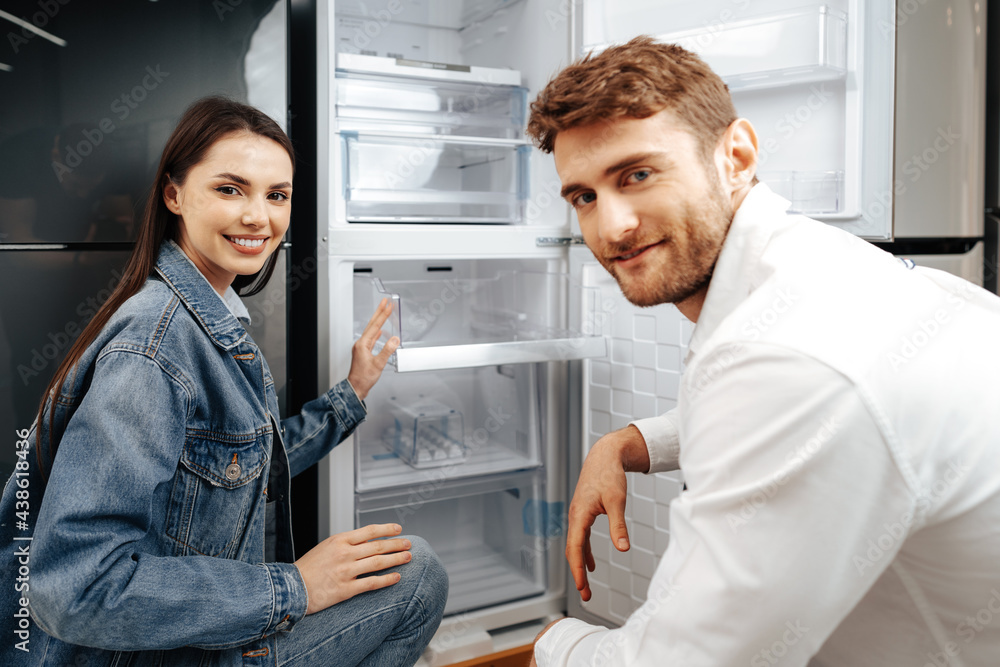 Fototapeta premium Young couple selecting new refrigerator in household appliance store
