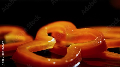 Slices of orandge bell pepper fall down on brown wooden board with water drops photo