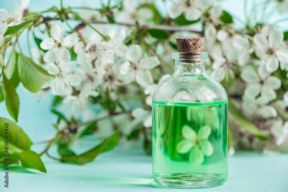 Bottle with natural cosmetic oil and flowers on blue background. Aromatherapy and spa wellness concept. Organic skin care product. Bottle with natural cosmetic oil and flowers on blue background. Aromatherapy and spa wellness concept. Organic skin care product.