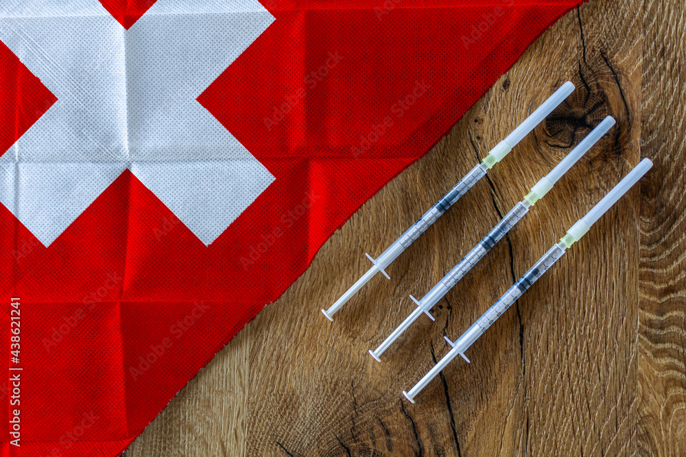 Concept of the ongoing efforts by Switzerland to deliver and distribute COVID-19 vaccines with three syringes on a wooden table ready to use with a Swiss Flag. Copy Space for Text and Graphics.