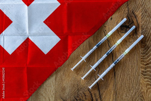 Obraz na płótnie Concept of the ongoing efforts by Switzerland to deliver and distribute COVID-19 vaccines with three syringes on a wooden table ready to use with a Swiss Flag. Copy Space for Text and Graphics. w salonie