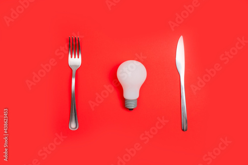 Romantic valentines day dinner idea concept. Light bulb on plate and silver wear on red background.