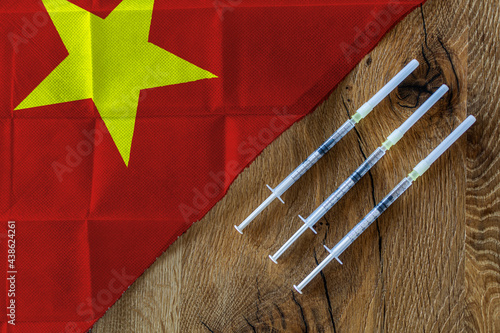 Concept of the ongoing efforts by Vietnam to deliver and distribute COVID-19 vaccines with three syringes on a wooden table ready to use with a Vietnamese Flag. Copy Space for Text and Graphics.