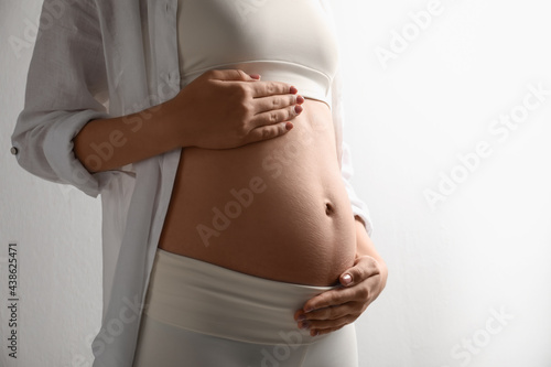 Pregnant young woman touching belly on light background, closeup. Space for text © New Africa