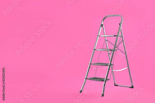 Modern metal stepladder on pink background. Space for text photo