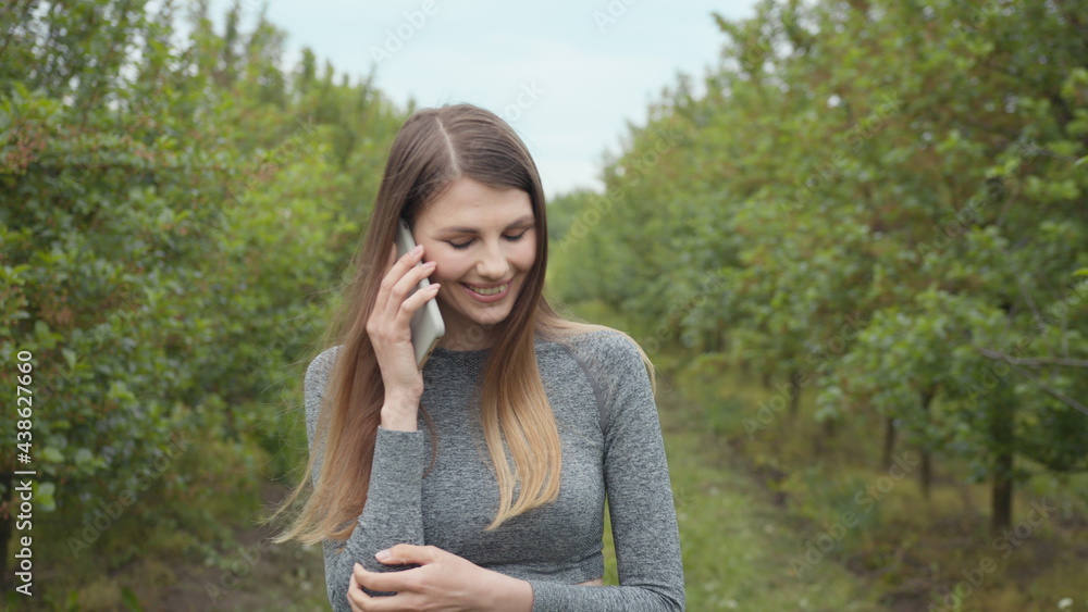 Happy hipster woman typing by mobile phone outdoors. Cheerful girl with smartphone in park on a background of trees. Smiling lady holding cellphone in hands outside. The girl communicates by phone Happy hipster woman typing by mobile phone outdoors. Cheerful girl with smartphone in park on a background of trees. Smiling lady holding cellphone in hands outside. The girl communicates by phone
