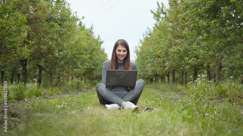 Girl sitting in park or forest, opening laptop on nature. IT specialist working at self isolation outdoors. Women engaging in business or freelance at nature or fresh air at amazing sun light. © GRAFStock