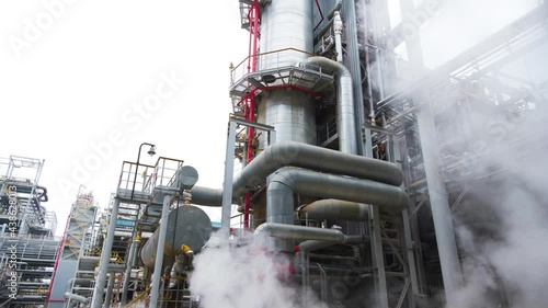 Moving through the clouds of thick steam at the site of an oil refinery. Huge steel pipes and pipelines on the background.