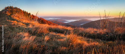 Panorama alpine landscape of the mountain peaks and valleys covered in fog at dawn. Autumn Landscape mountains and colorful forest on background sunrise.