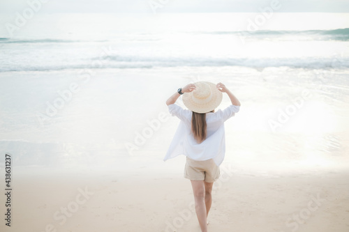 Back view of Young girl wearing white t-shirt and hat walks at beach. Girl in a white t-shirt on the background of the ocean. Summer travel concept.