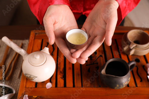 Master offering cup of freshly brewed tea during traditional ceremony at table, closeup photo