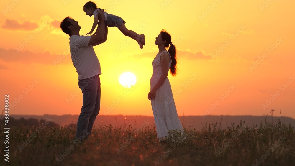 Happy family plays in summer park at sunset. Dad throws his beloved daughter up, happy child laughs and rejoices, hugs dad outdoor. Child, father, mom. Father and daughter play, dreams of flying